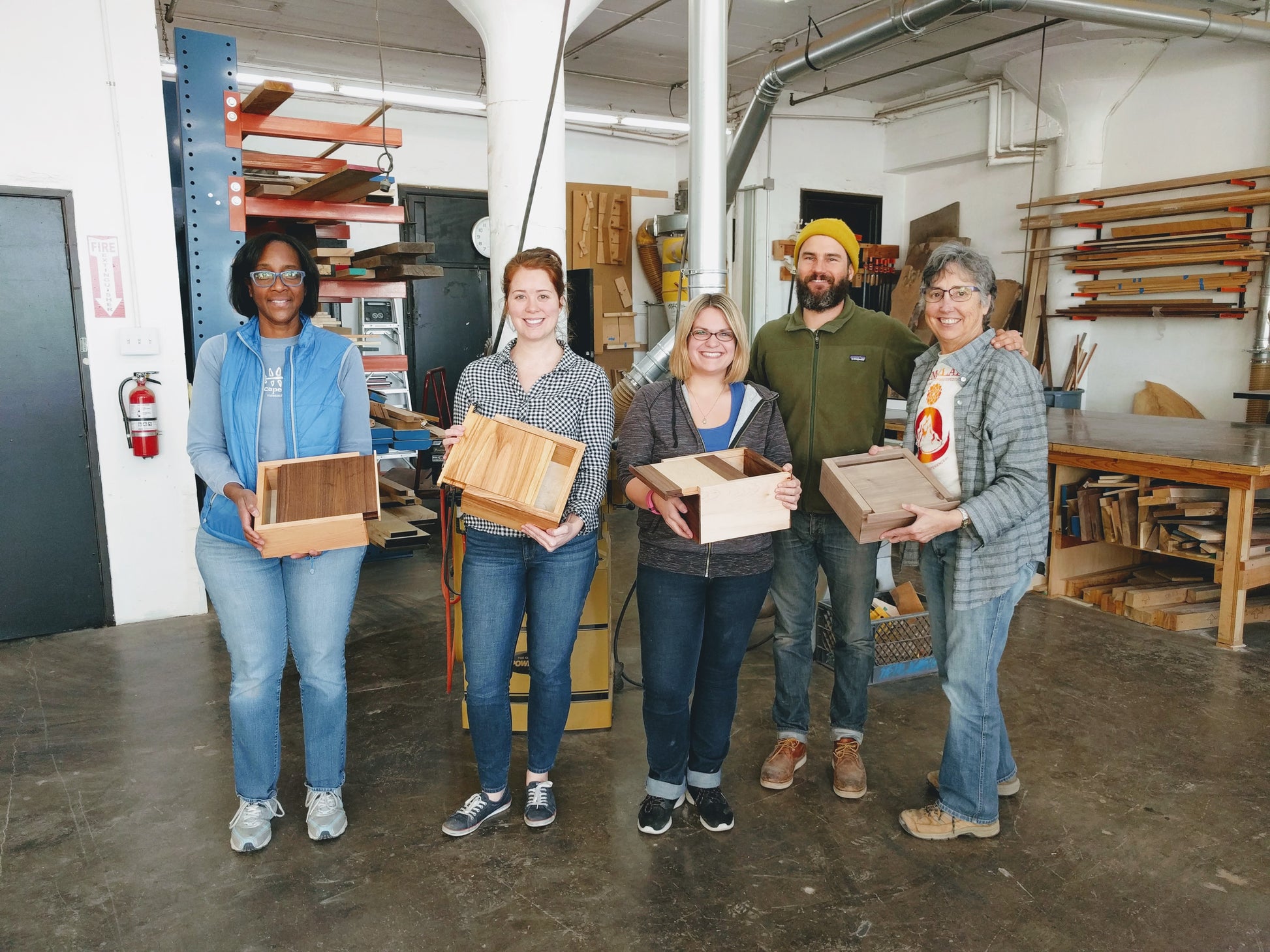 Woodworking students happily hold up their finished handmade boxes in the shop