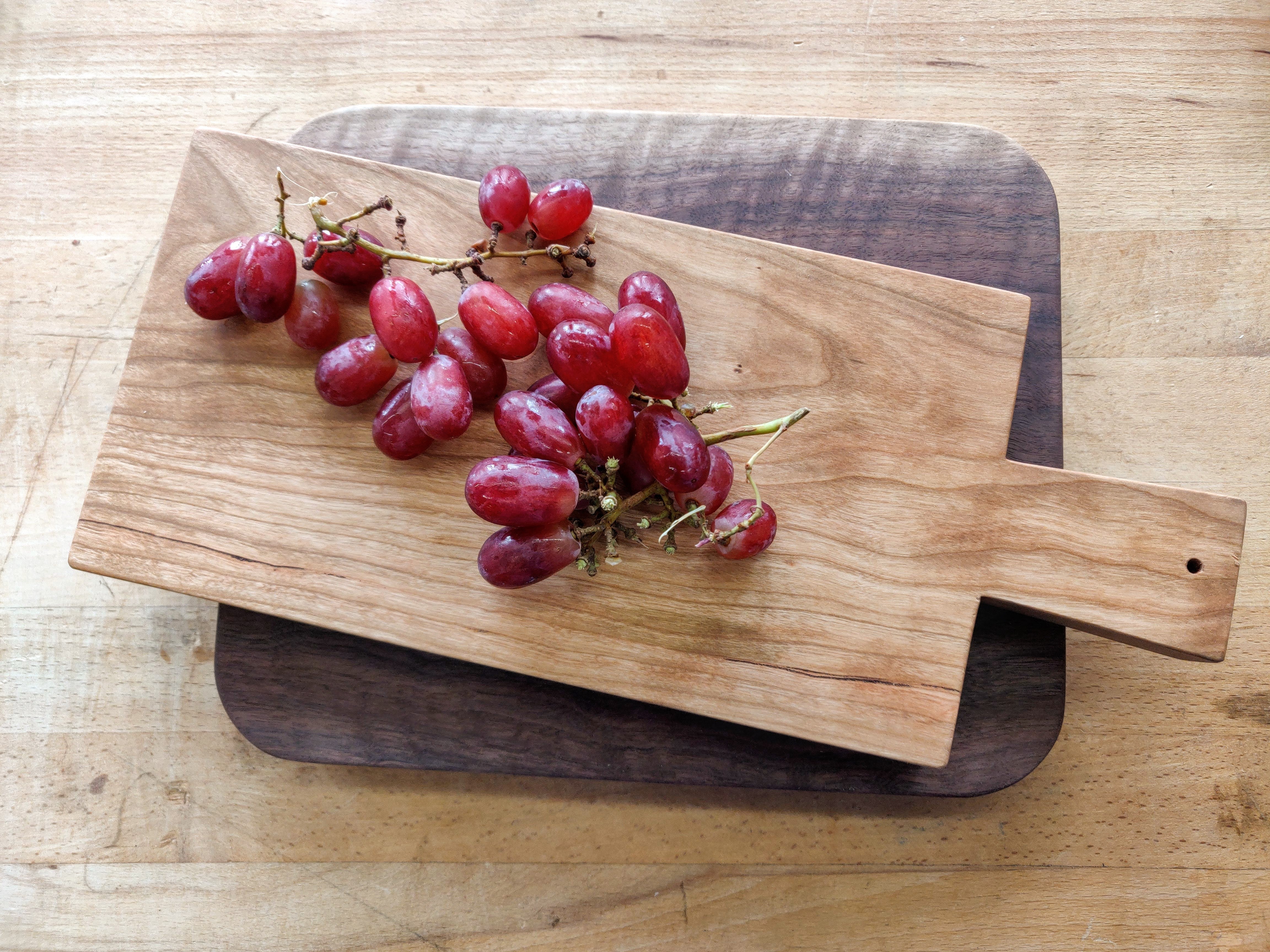 Two bunches of red grapes lay on a stack of handmade cutting boards